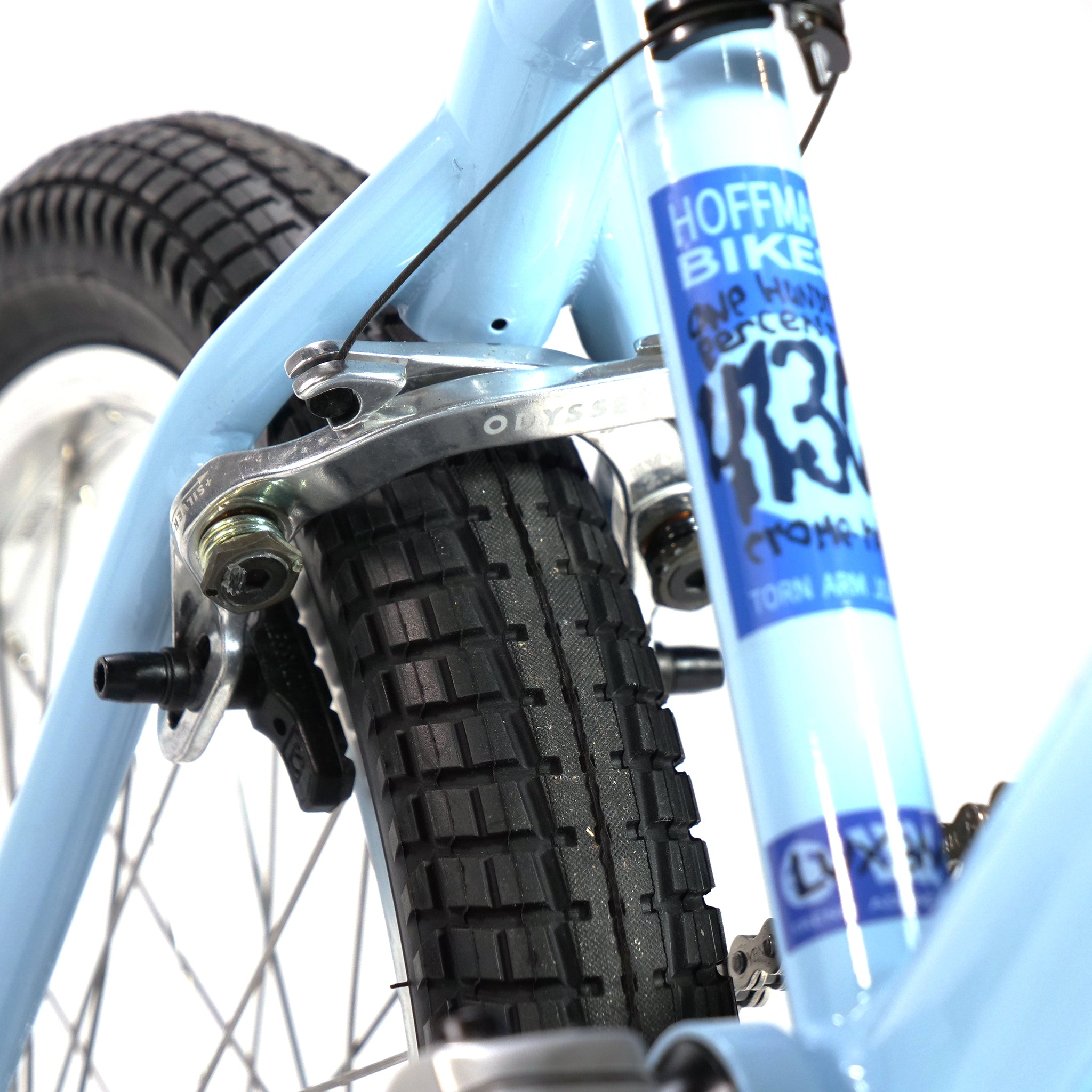 Close-up of the rear tire, brake assembly, and frame of a blue Hoffman TAJ Trend Adjacent Joy 20 Inch Custom BMX bike, adorned with branding stickers. Ideal for freestyle enthusiasts inspired by legends like Taj Mihelich.