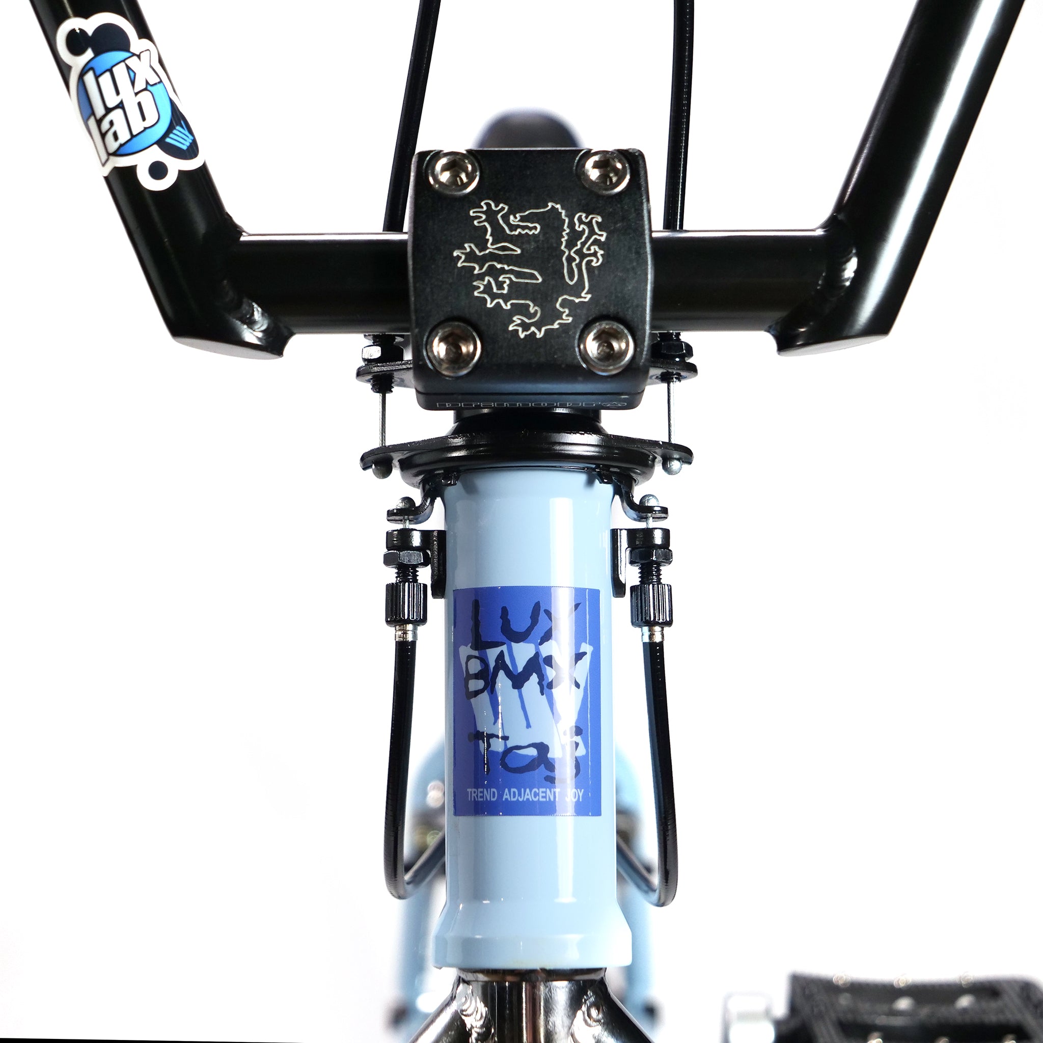 Close-up of Hoffman TAJ Trend Adjacent Joy 20 Inch Custom Bike's handlebar and stem, featuring a blue frame and black grips. A logo, reminiscent of Hoffman Bikes or Taj Mihelich's designs, is visible on the frame and stem.