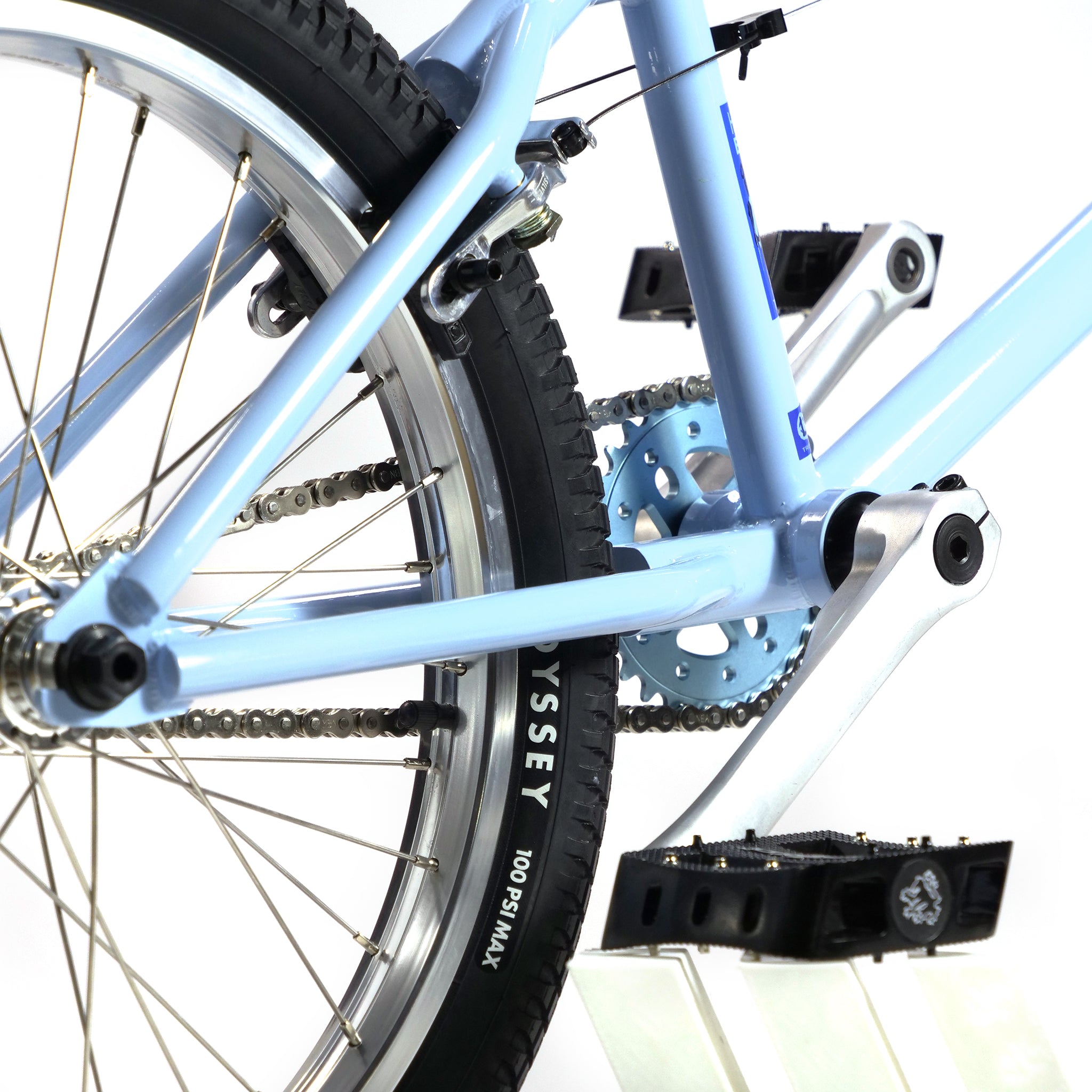 Close-up of the Hoffman TAJ Trend Adjacent Joy 20 Inch Custom Bike's rear wheel and frame, displaying the chain, gears, and pedal. On a stand, this blue BMX freestyle bike is reminiscent of a Hoffman classic and ready for action.