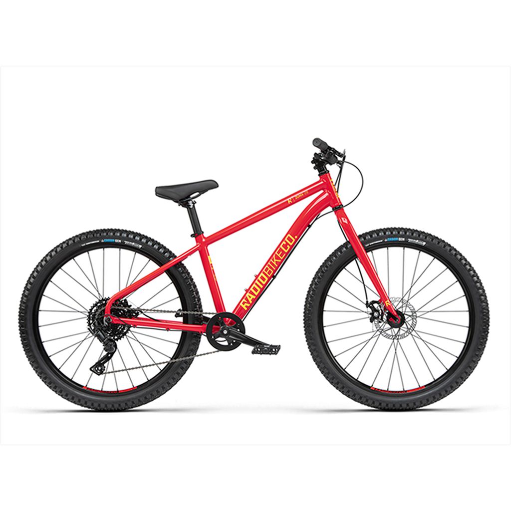 The Radio 26 Inch Zuma Bike, a kids MTB bike with a lightweight alloy frame, features a striking red color with black tires and a black seat. This mountain bike is equipped with disc brakes, a rear derailleur gear system, and proudly displays "RADIOBIKES" on the frame.