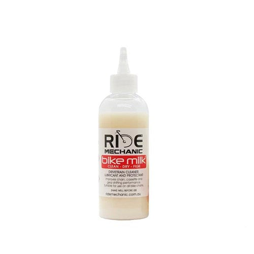 The Ride Mechanic Bike Milk is a multifunctional product combining a drivetrain cleaner, lubricant, and protective film, all packaged in a bottle with a white nozzle cap and adorned with a red label featuring black text.