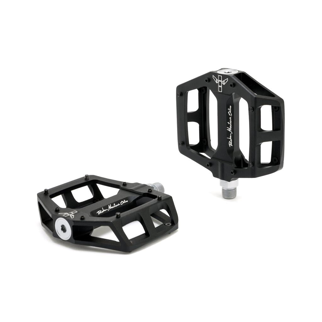 The Fly Bikes Ruben Aluminum Pedals feature a geometric design in black with a CNC Chromoly axle and precision bearings for smooth rotation, presented on a white background.