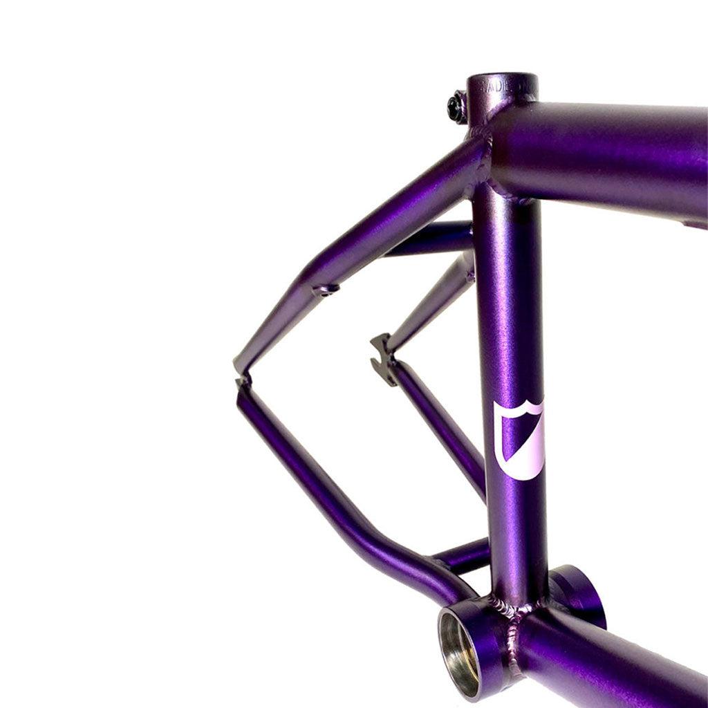 A close-up view of a partially assembled Purple Haze Colorway bicycle frame with a white shield logo on the front, showcasing the responsiveness and stability of the ATF XL (Aryei Levenson) Frame.