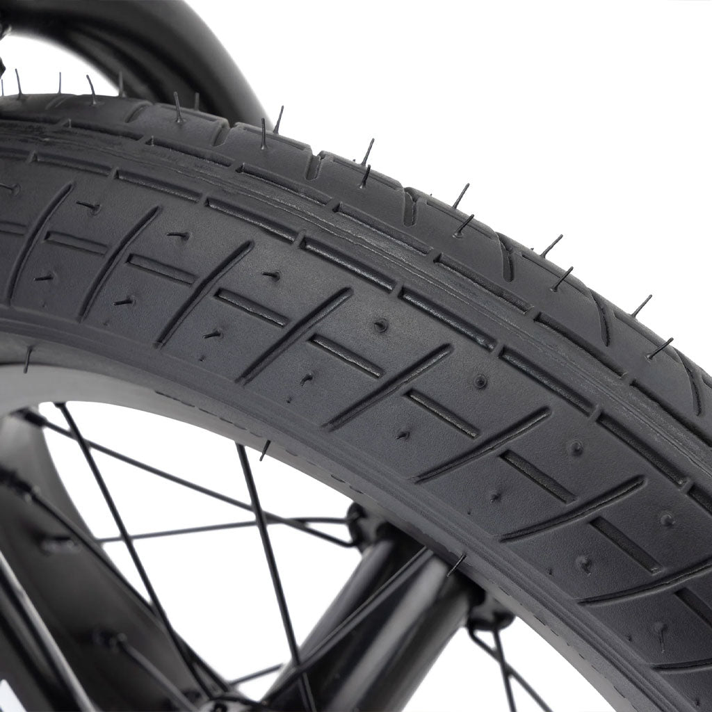 Close-up image of a bicycle tire with visible tread pattern and spokes of the wheel in the background, showcasing the sturdy 12” wheels of a Kink Roaster 12 inch Bike (2025).