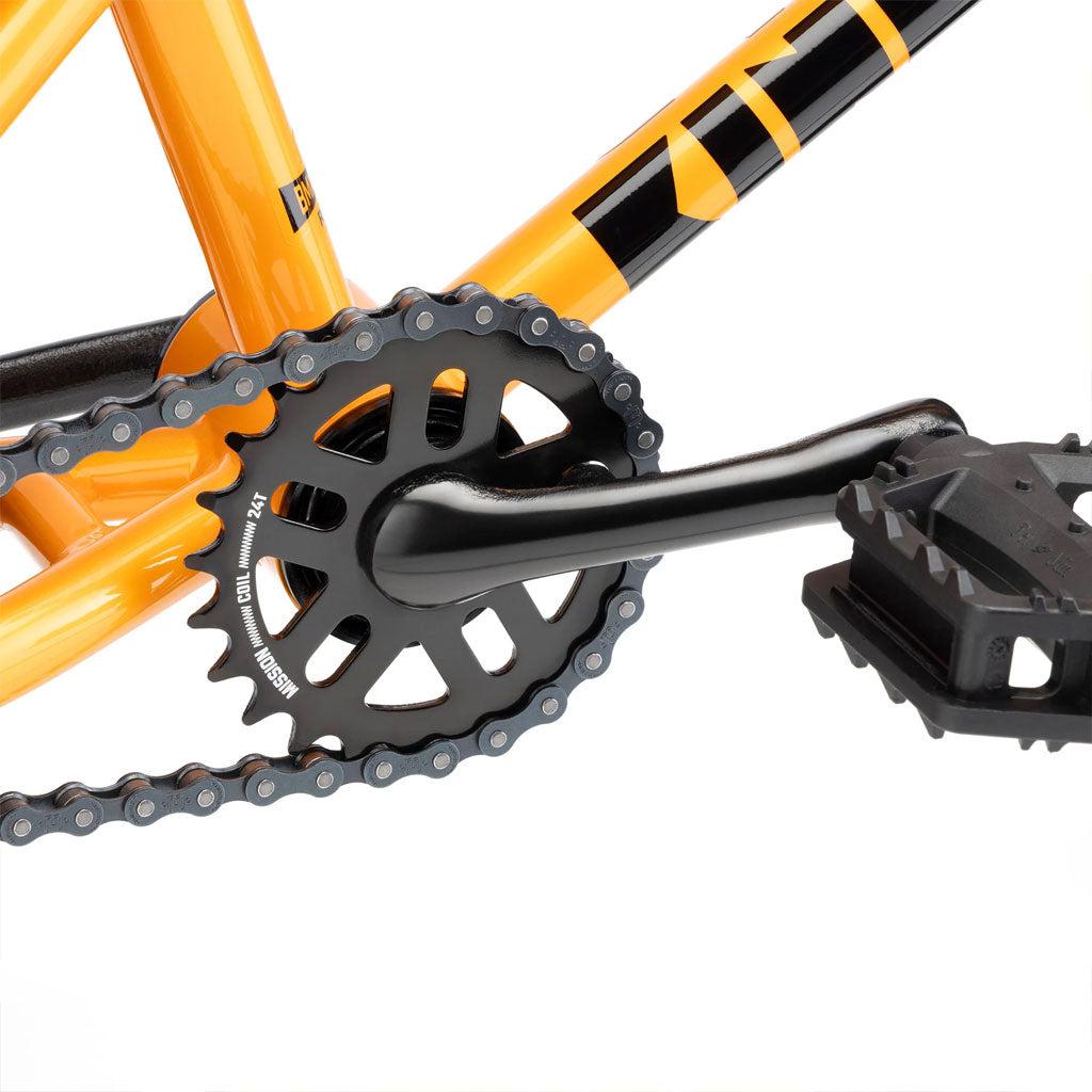 Close-up of a bicycle crankset, featuring a black crank arm, chainring, and pedal connected to an orange bike frame with 12” wheels—perfect for a child's first Kink Roaster 12 inch Bike (2025).