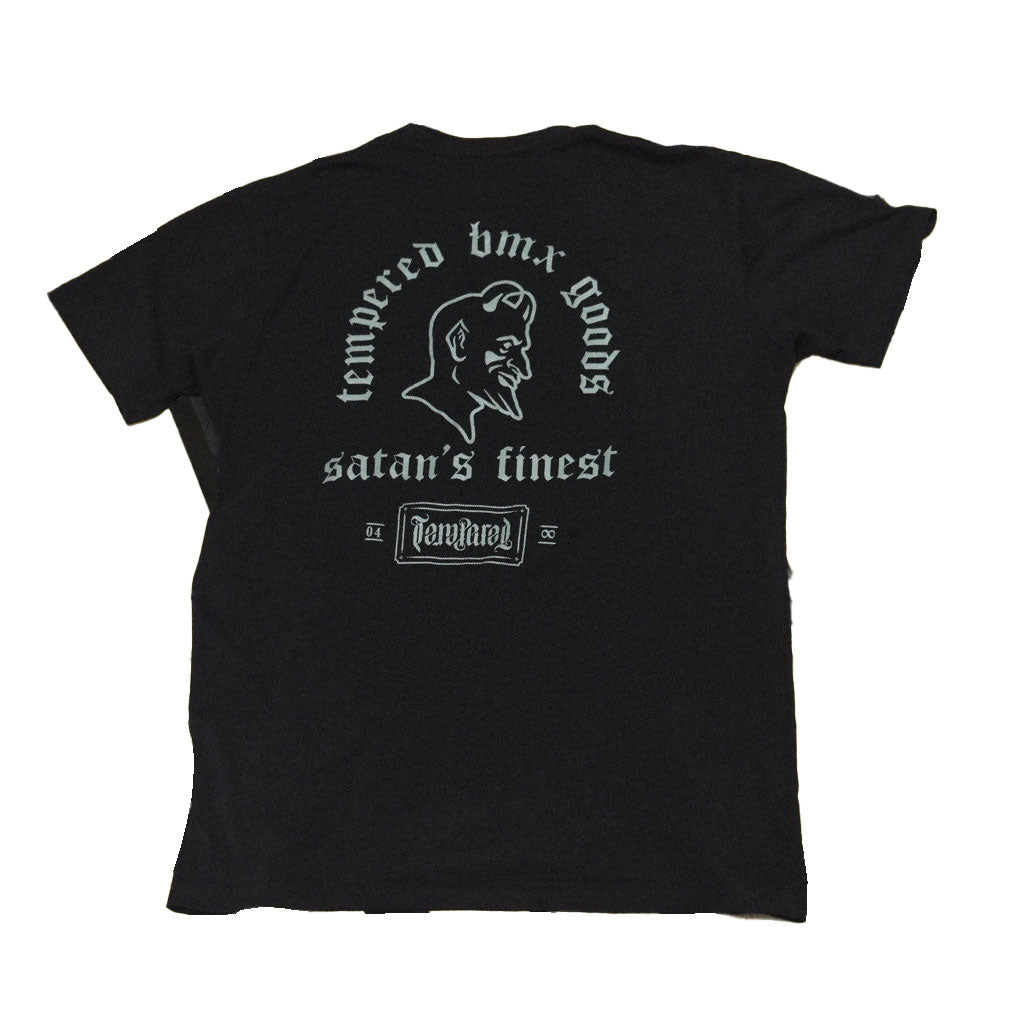 The Tempered Goods Satan's Finest Tee features a black color with white text, showcasing "Tempered BMX goods" on the back, "Satan's Finest" above a devil illustration, and "Tampered" at the bottom. It's designed for those who value handmade quality and edgy style.