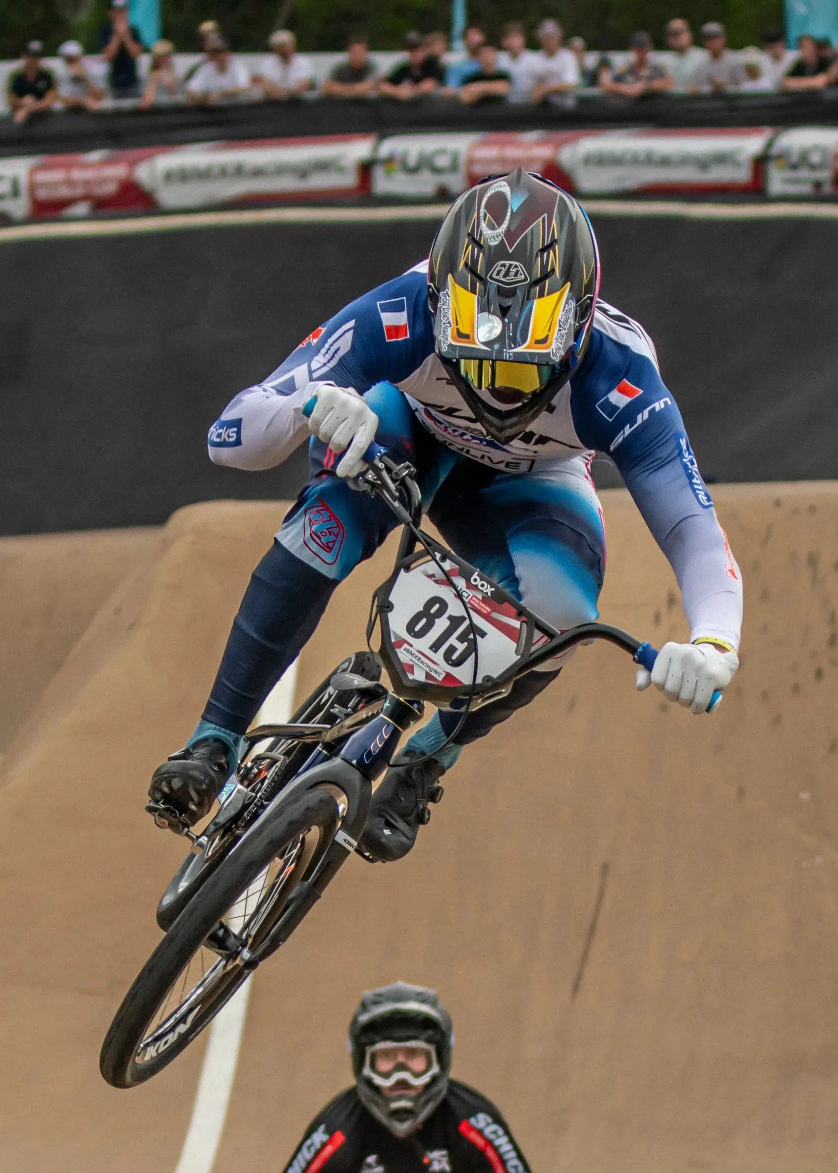 A BMX rider wearing a blue and white suit and a full-face helmet soars mid-air during the 2024 National BMX Championships in Perth, perfectly captured in this LUXBMX Race Photo Package. Another rider is visible below in the background, highlighting the thrilling competition.