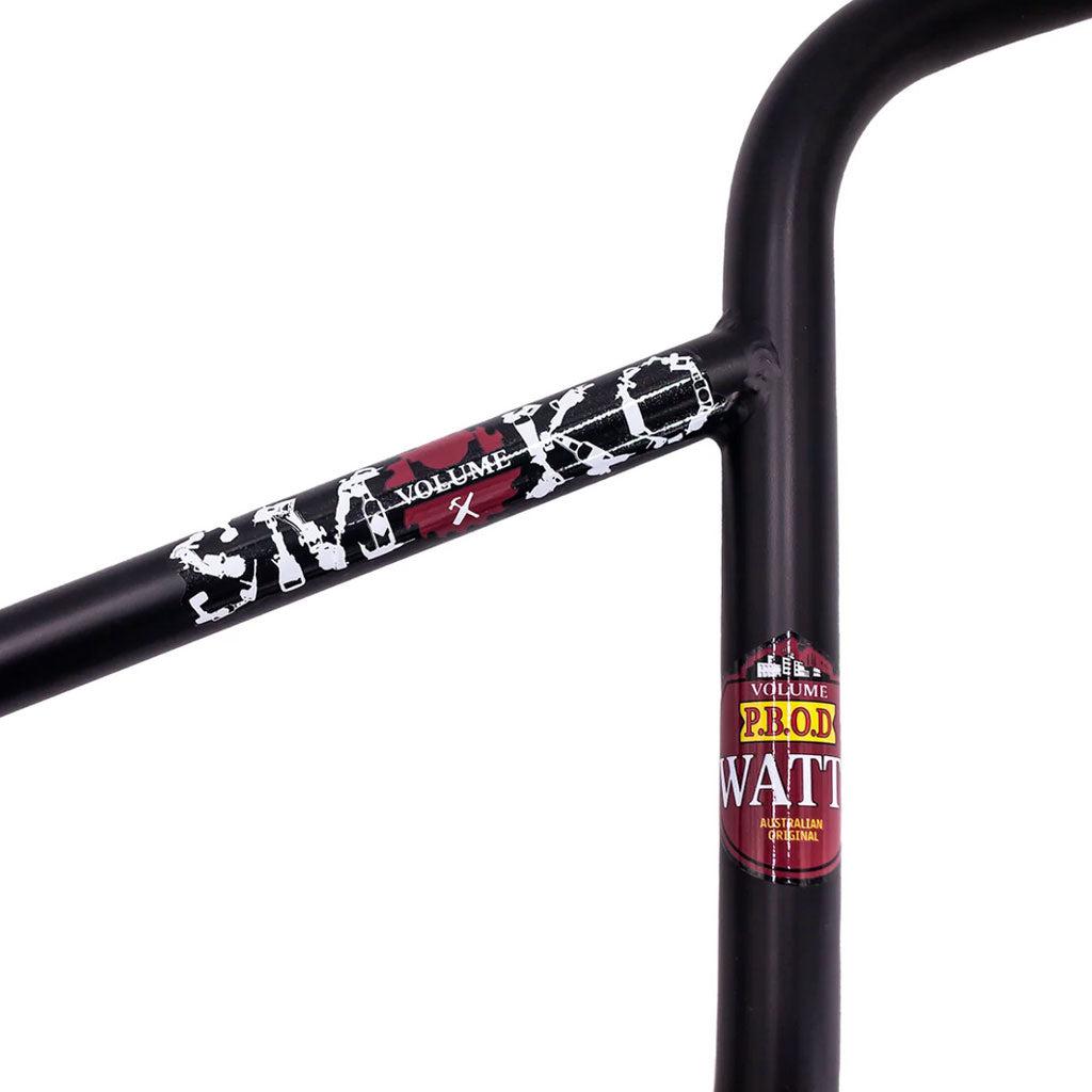 Close-up of the Volume Jason Watts Smoko Bar in black, showcasing the "SMOKO" text and two vibrant stickers—one red and white, the other red and yellow. Made from heat-treated chromoly, these signature bars offer durability and style for any biking enthusiast.