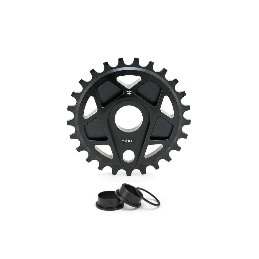 The Fly Bikes Tractor XL Sprocket is a black 25-tooth bicycle sprocket, expertly CNC machined from 6061 Aluminum, featuring three circular cutouts and two small black spacers.