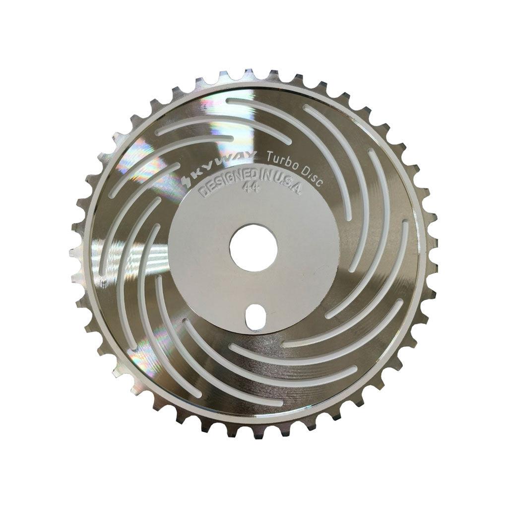 A close-up of a metallic circular saw blade with evenly spaced teeth around the edge and spiral grooves on the surface, labeled as "SKYWAY Turbo Disc Designed in U.S.A." This Skyway Turbo Disc Front Sprocket is precision-engineered from CNC machined 6061 Aluminum.