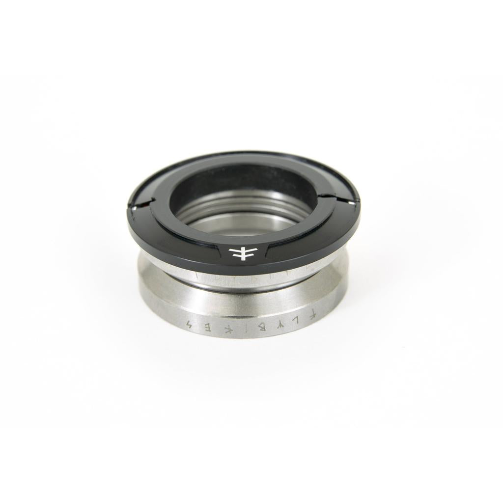 A sleek metallic and black camera lens adapter ring, reminiscent of the Fly Bikes Volcano Headset's design, rests on a pristine white background.