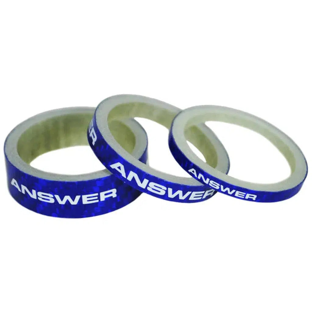 Three rolls of blue tape, each precisely matching the stack height of the Answer Mini 1in Carbon Headset Spacer set, have the word "ANSWER" printed on them and are arranged side by side.