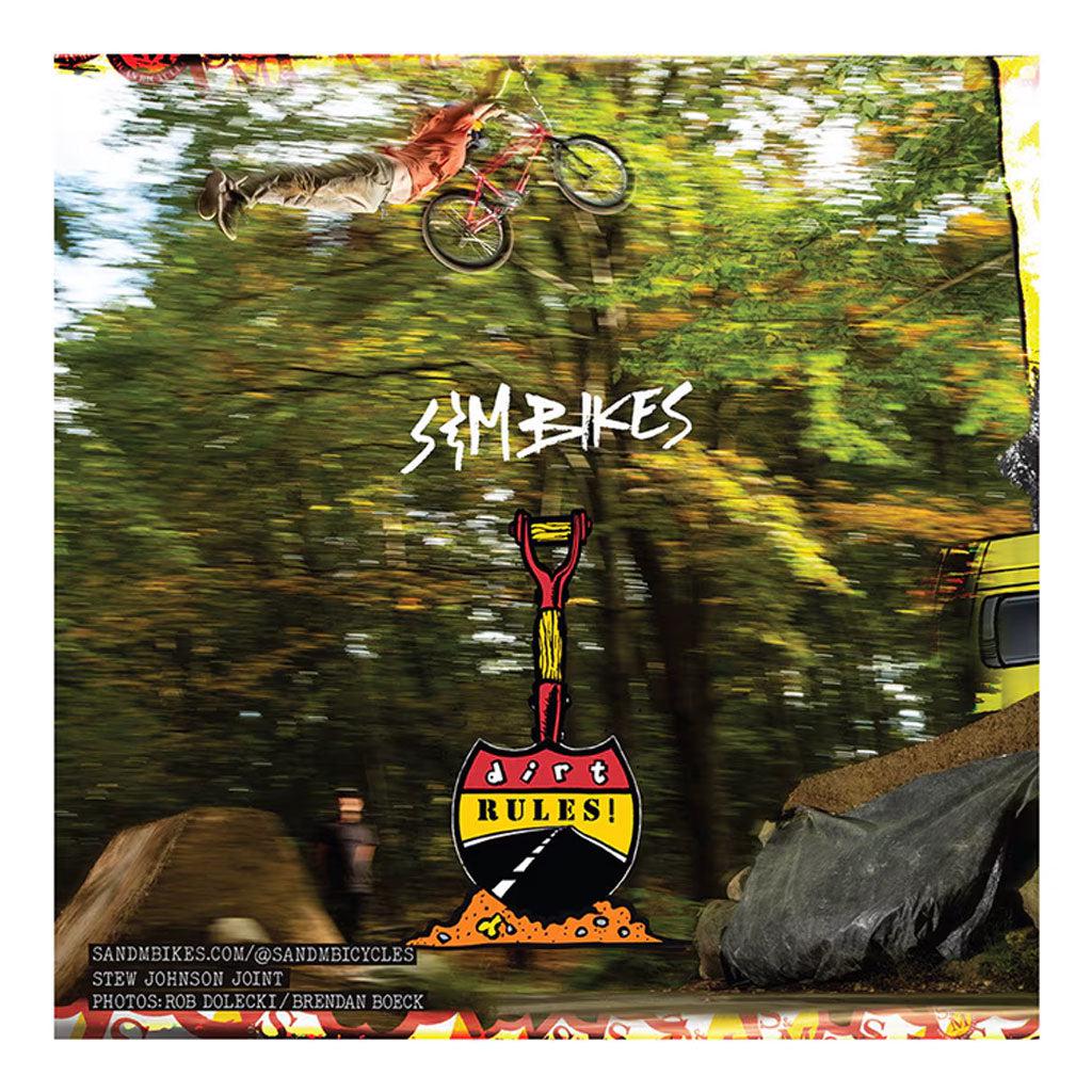 A cyclist is airborne over a dirt jump surrounded by trees. Text reads "S&M Aussie Rules" and "Dirt Rules" with a shovel design. Experience the thrill of BMX events and discover more about the S&M Aussie Rules DVD below. Contact details and credits are listed below.