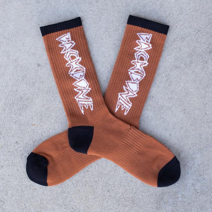 The Backbone Crew Socks, buttery soft with black toes and heels, feature white jagged text along the sides in a crisscross pattern on a gray surface. One size fits most.