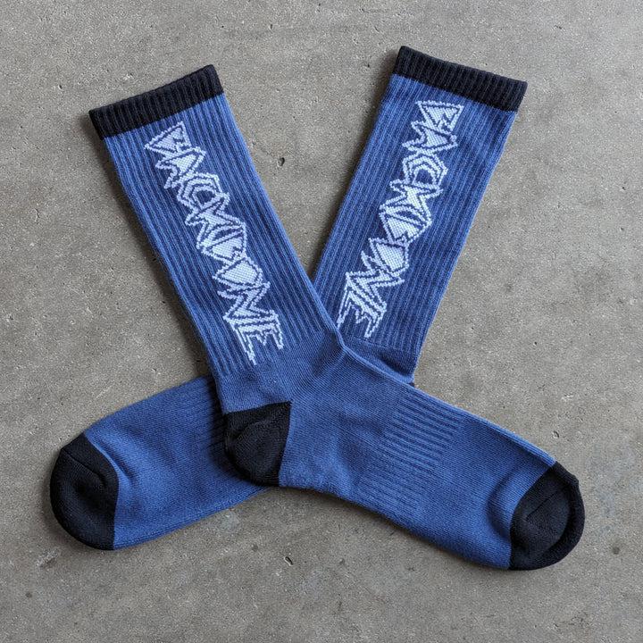 The Backbone Crew Socks are blue with black heels and toes, boasting a buttery soft feel. Adorned with "BACKBONE" in a jagged, repeating side pattern, these one-size-fits-most socks effortlessly blend comfort and style.