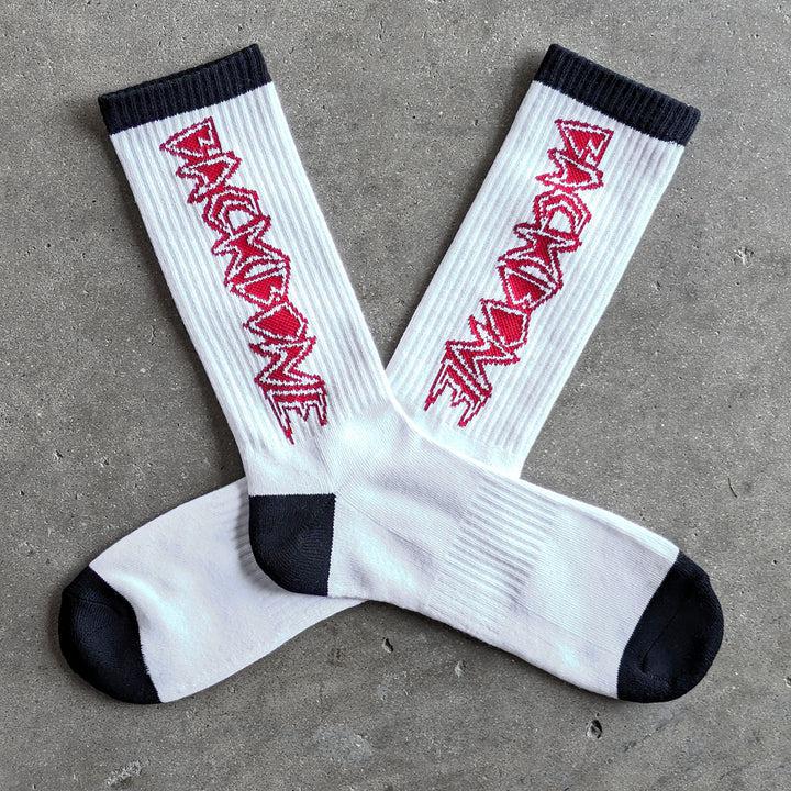 Backbone Crew Socks are white with a buttery soft feel, featuring a black toe and heel, and red "BACKBONE" text on the sides. They're laid out on a concrete surface and designed to be one size fits most.