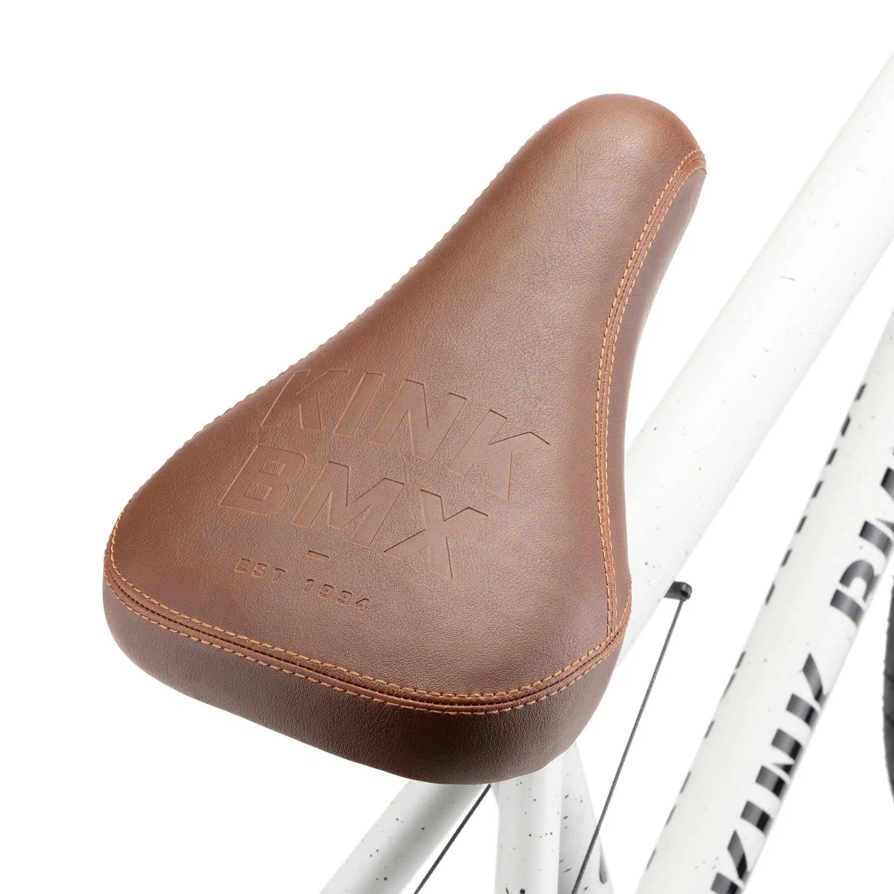 Brown leather seat with embossed "KINK BMX" and "EST. 1994" lettering, mounted on the durable 4130 Chromoly frame of a Kink Gap XL 20 Inch Bike, featuring a sleek white design.