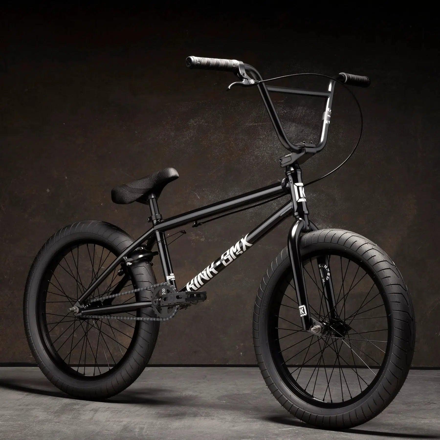 A Kink Launch in black, featuring thick tires and a simple design, is set against a dark background, highlighting the classic sleekness of this 20-inch BMX bike.