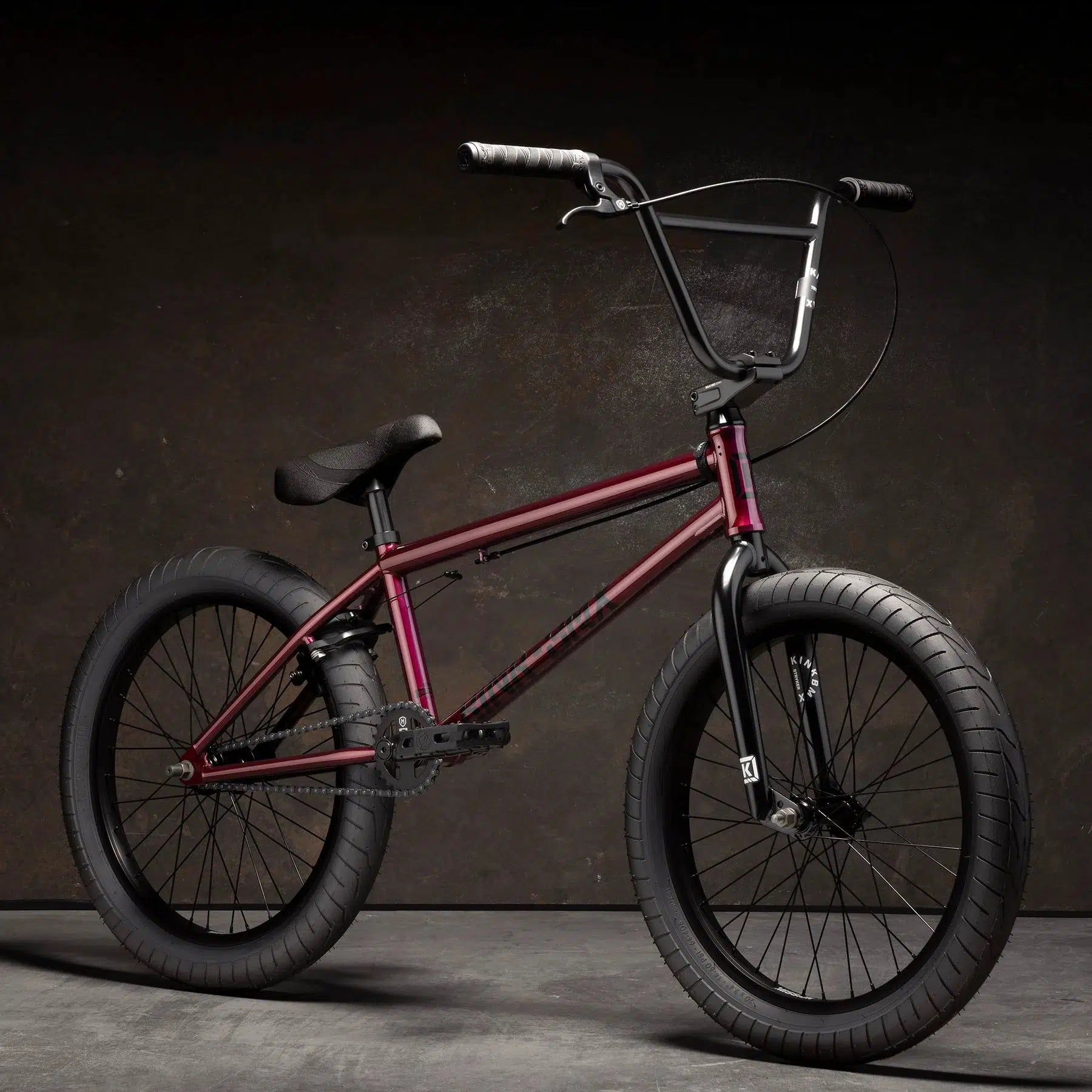 A Kink Launch 20 Inch Bike in red, featuring thick black tires, is displayed against a dark background.