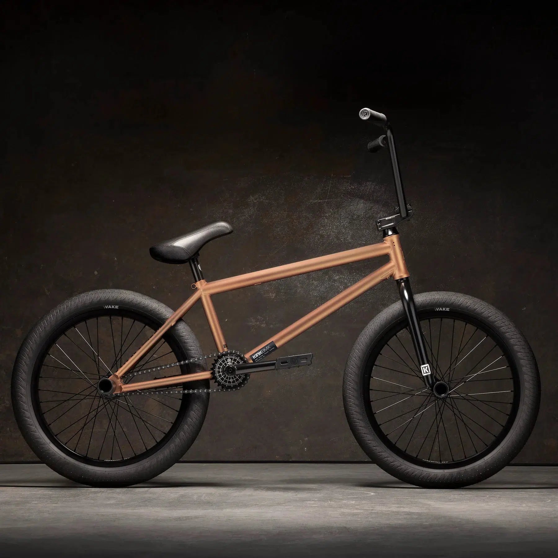 The Kink Switch 20 Inch Bike boasts a copper-colored Chromoly frame from Kink BMX, complemented by black handlebars, seat, tires, and a freecoaster hub set against a dark background.