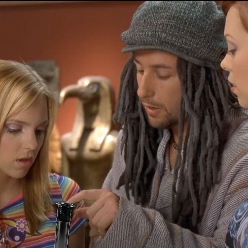 Three individuals examine a small object, with the person in the center, wearing a beanie and dreadlocks, pointing at it—the cleverly concealed Salt Plus Bunker M24 Fork Preload Bolt. In the background, there is a statue resembling an Egyptian figure.