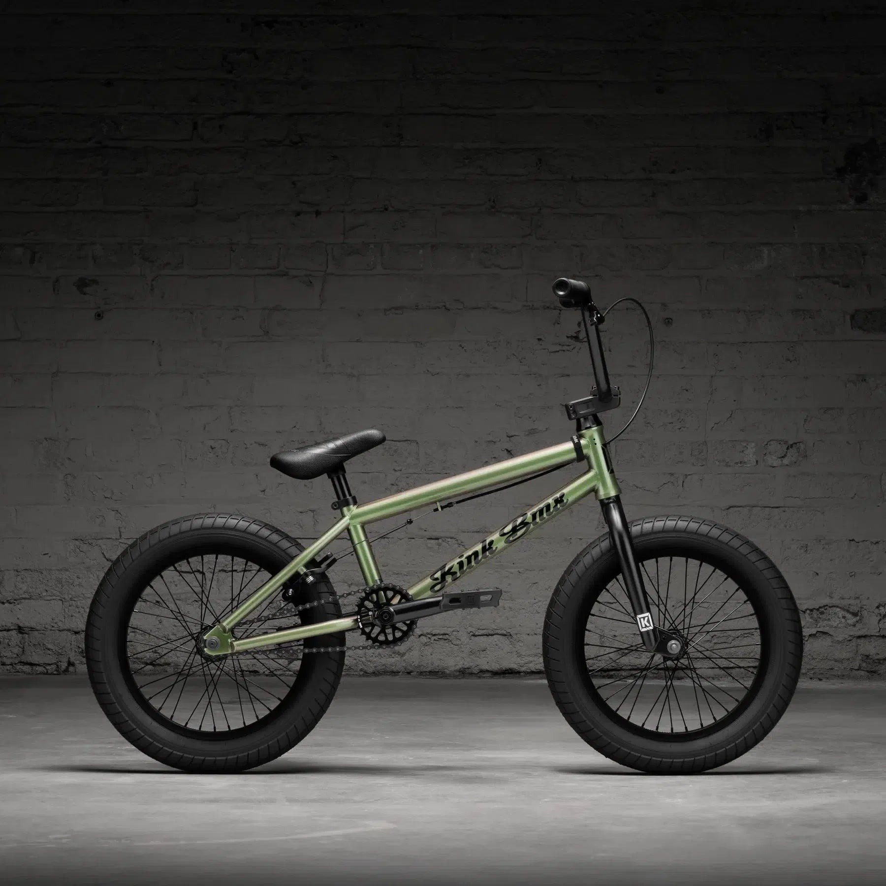 The 2026 Kink Carve 16-inch bike, featuring a green frame with black tires and handlebars, is displayed against a textured gray brick wall.