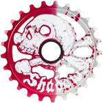 The Shadow Conspiracy Cranium Sprocket is expertly crafted from durable 7075 alloy, featuring a stylized skull design accented with white and red splatters. The word "Shadow" is elegantly written in stylized text at the bottom. The sprocket's left half showcases a striking bold red, while the right half gleams in silver.