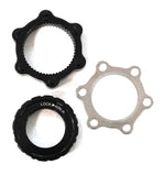 Three mechanical components from the Bengal Centerlock ISO Adapter Kit—a black circular piece with protrusions, a hexagonal ring with internal threads resembling a Centerlock style hub, and a silver circular disc with multiple holes like those found on a 6 bolt ISO disc rotor—laid on a white background.