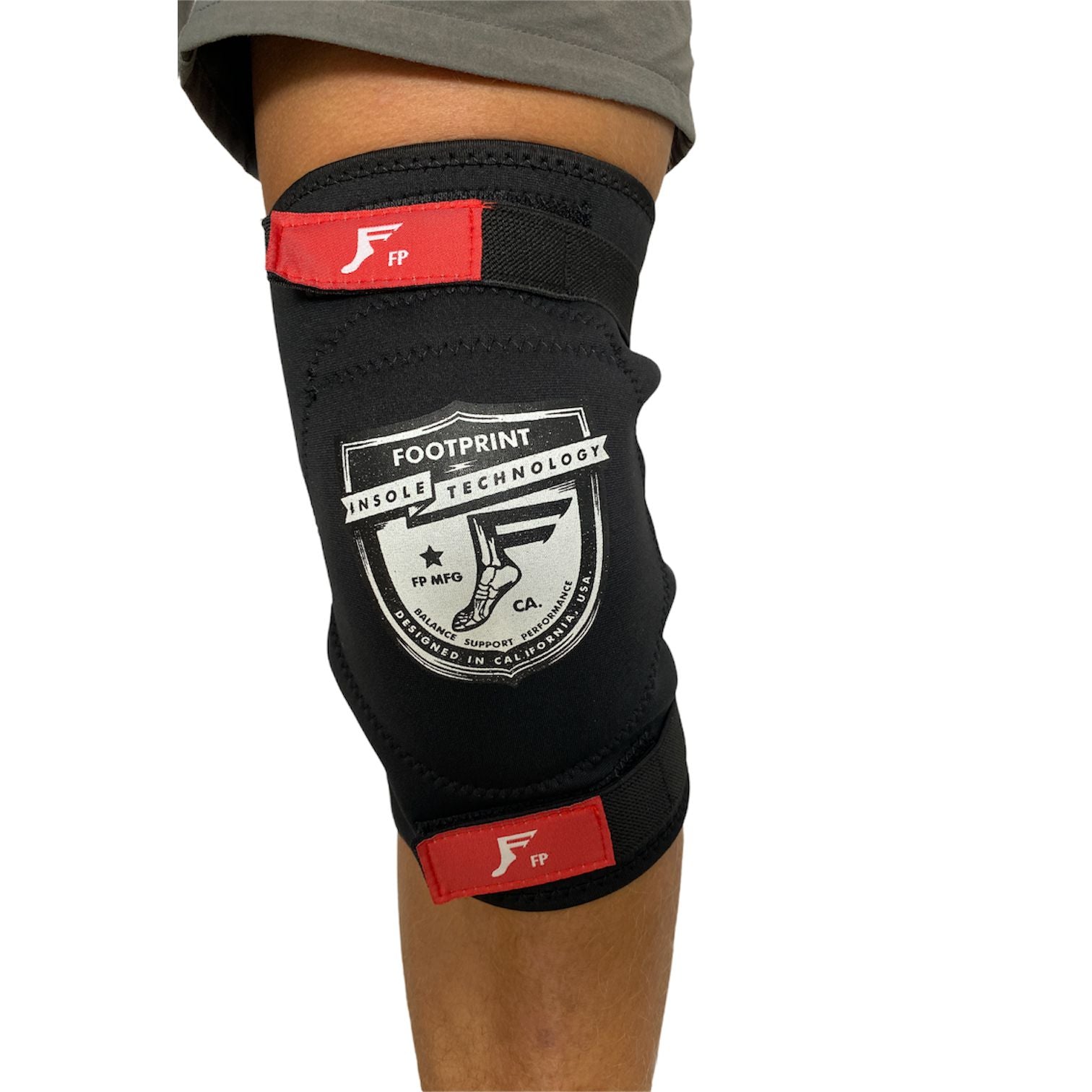 A person wearing a black FP Knee Street Protector Pads (Single) with adjustable red straps, featuring the Footprint Insole Technology logo for joint pains prevention.