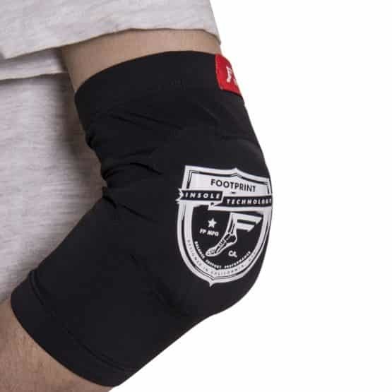 A person dressed in a light gray shirt wears a black and white elbow pad showcasing the Footprint Insoles Technology logo, highlighting the soft and flexible protection of FP Lo Pro Protector Elbow Sleeves (Pair).