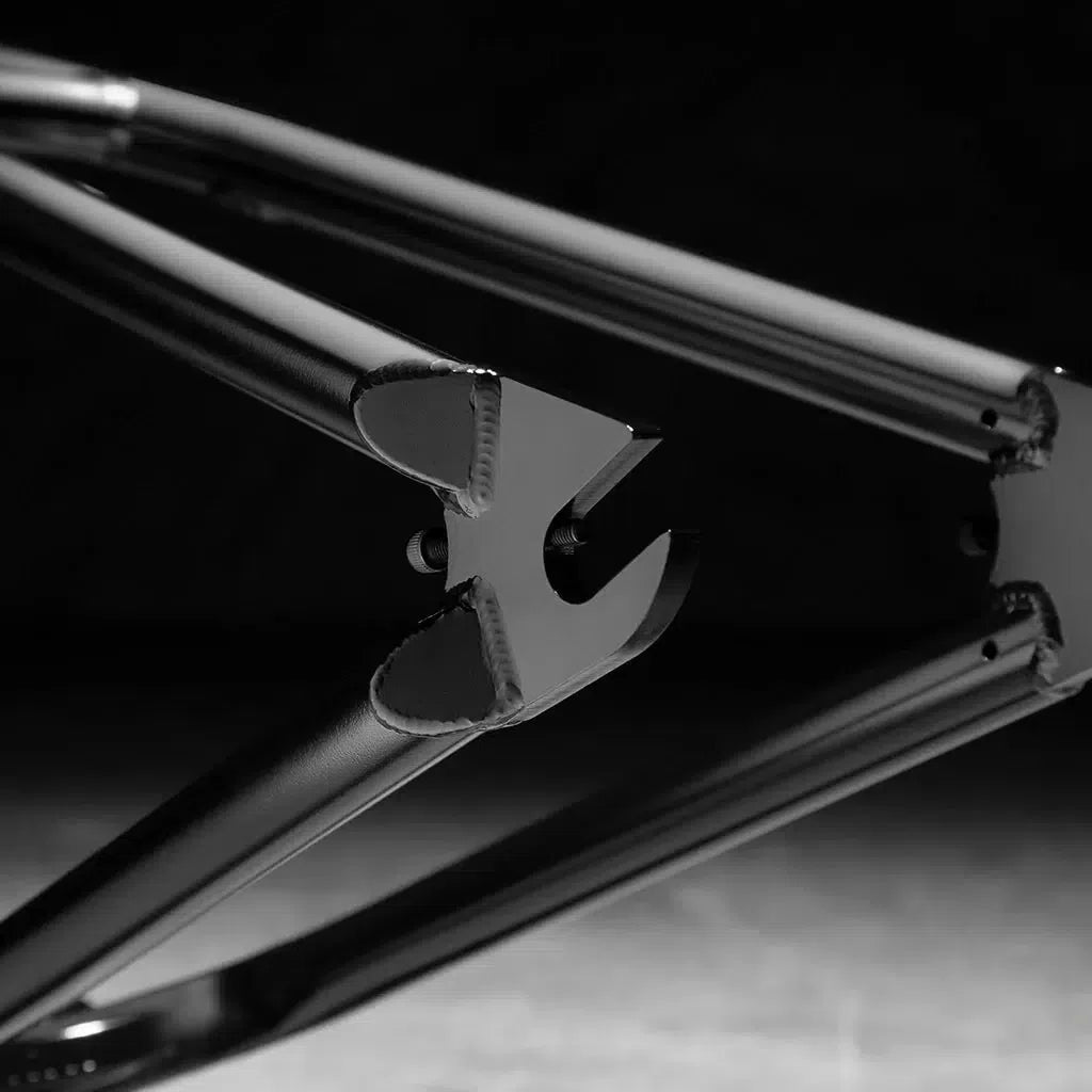 A close-up of the Kink Crosscut Frame dropout in black and white showcases precise metalwork, smooth welds, and modern geometry with integrated chain tensioners, all set against a dark background.