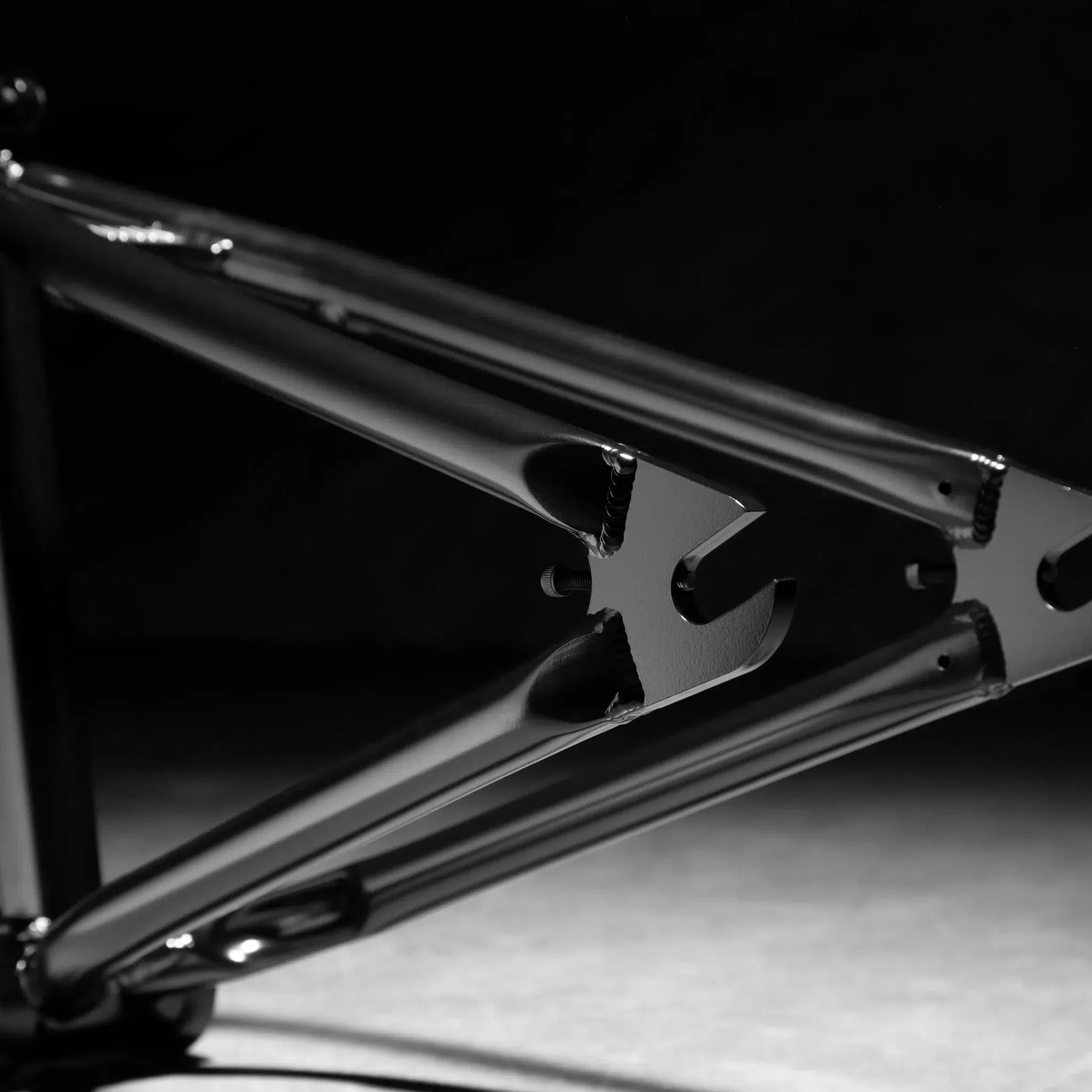 Close-up of a Kink Royale Frame, made from 4130 chromoly tubing, highlights its geometric design and structural details with built-in chain tensioners against a dark background.