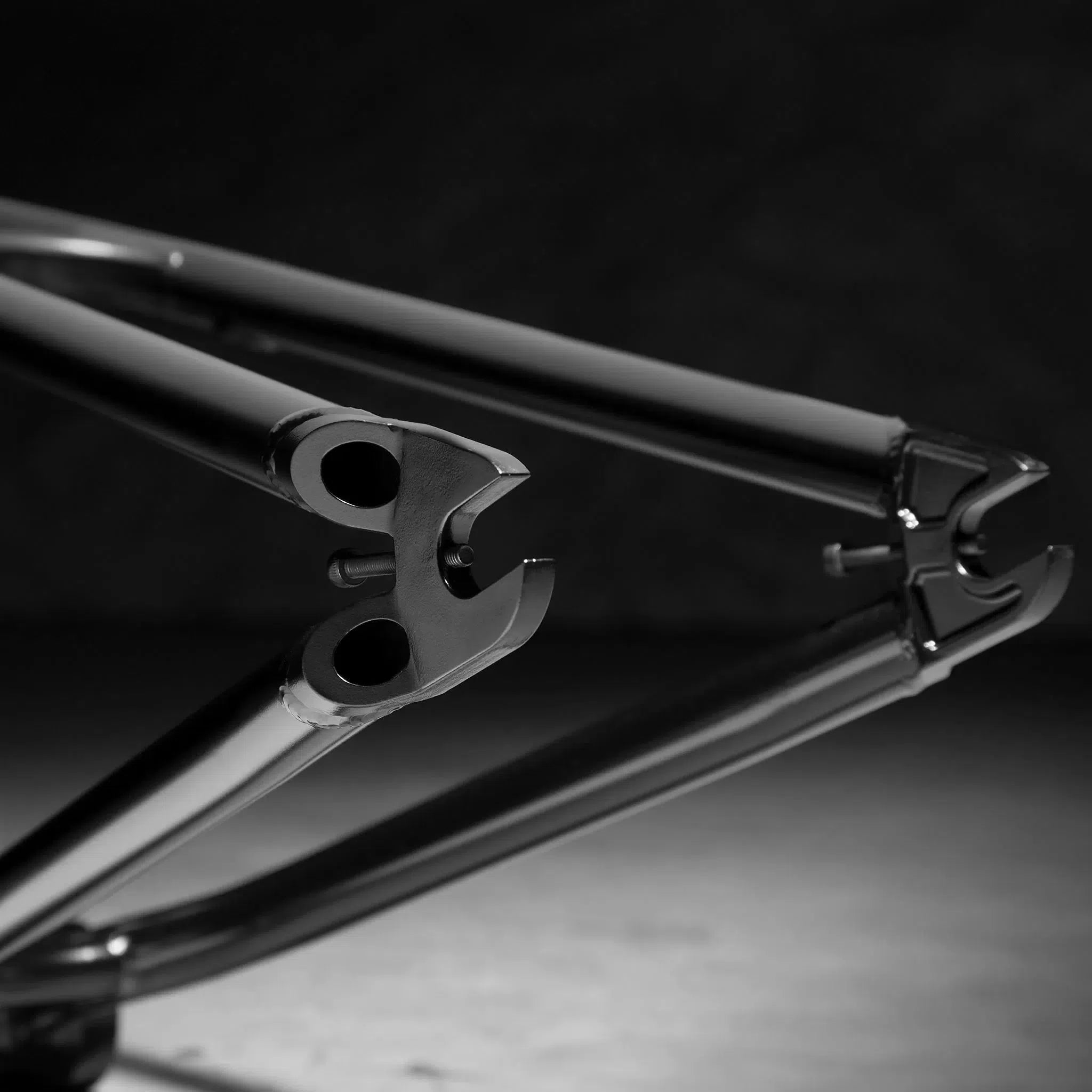 A close-up of the Kink Tactic Frame, showcasing its chromoly tubing, rear dropouts, and chain stays on a smooth surface in a monochromatic setting.