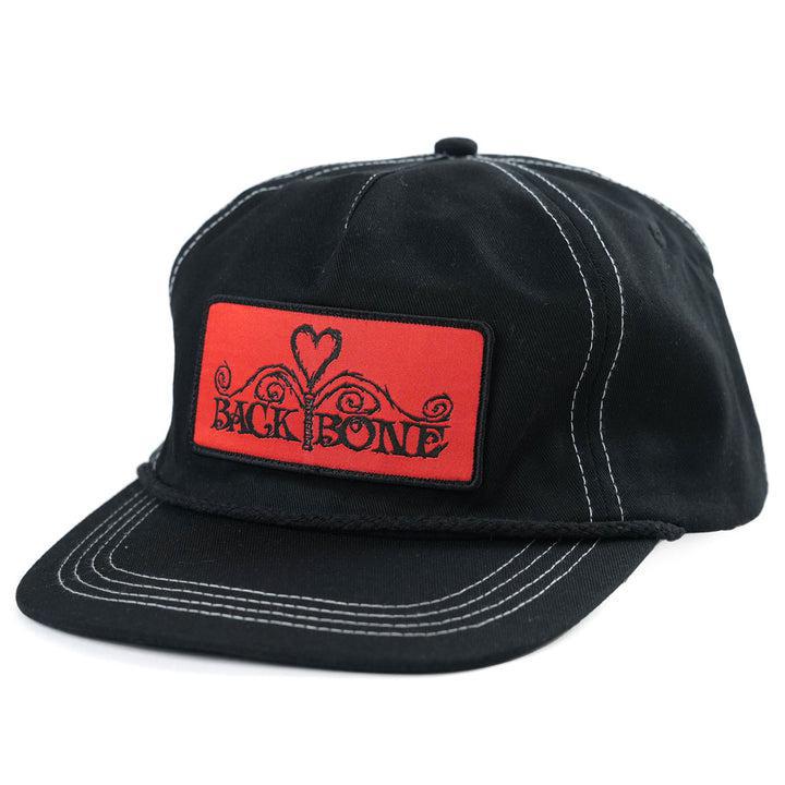 The Backbone Heart Logo 5 Panel Hat features white stitching and a red front patch with a heart design. "Back Bone" is prominently displayed in bold black letters, honoring the logo's legacy.