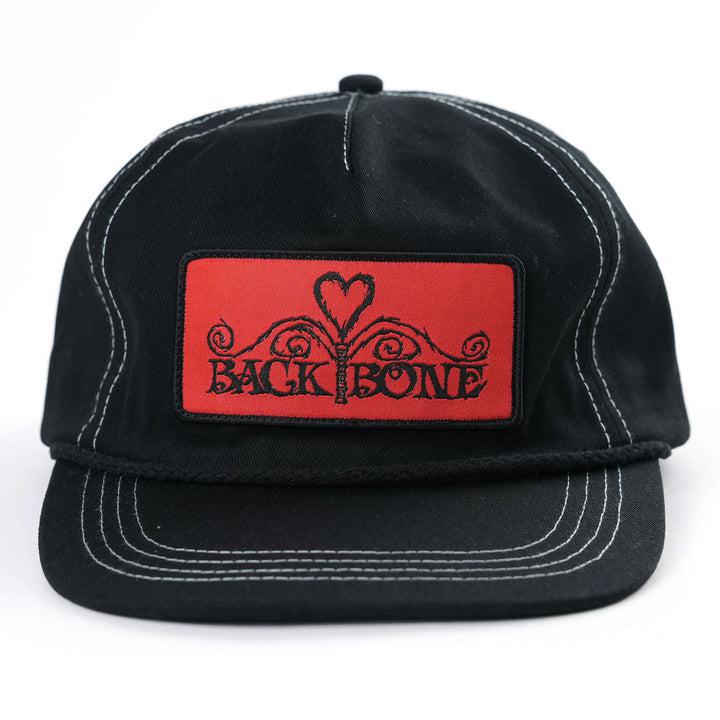 The Backbone Heart Logo 5 Panel Hat is black with white stitching, a red patch featuring a heart design, and "BACK BONE" text in an Aussie BMX style.