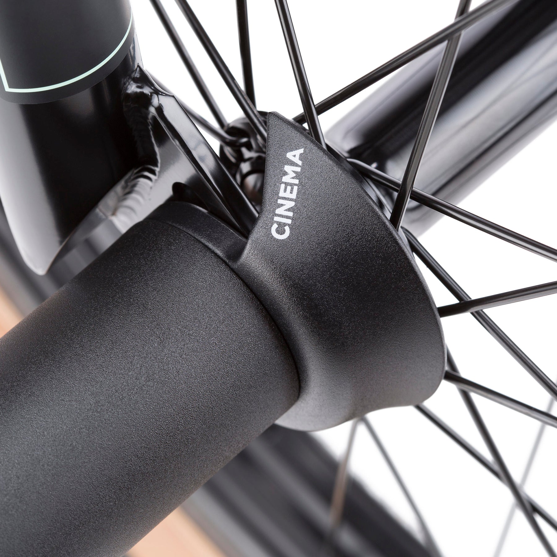 Close-up of a black bicycle wheel and fork, showcasing the Cinema VF Universal Front Hub Guard made from nylon composite over the axle, with visible spokes and part of the frame.