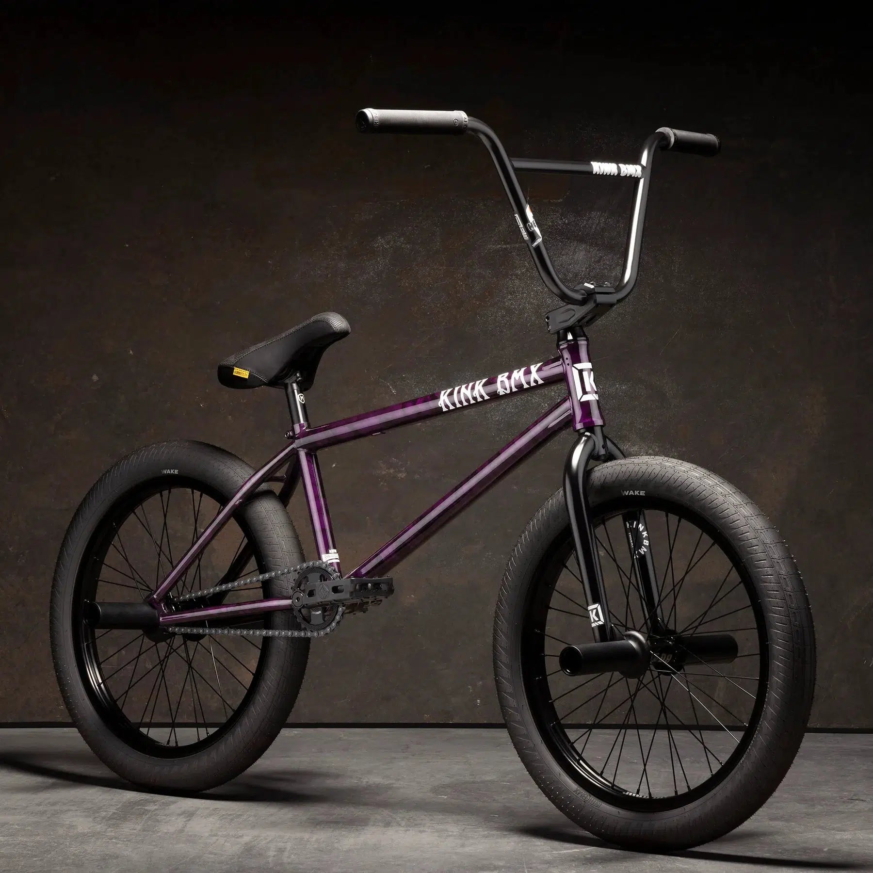 A Kink Downside 20 Inch Bike in purple, featuring black tires and handlebars, with modern geometry and crafted from 100% 4130 Chromoly, displayed against a dark, textured background.