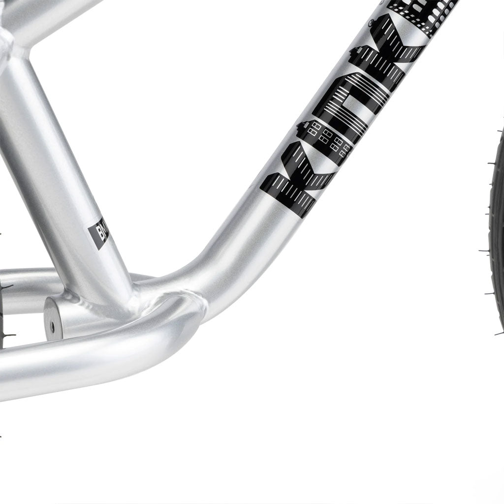 Close-up of a silver BMX balance bike frame with black geometric patterns, showcasing the sleek design of the Kink Coast Balance Bike model and part of the rear wheel.