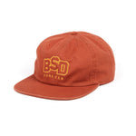 A rust-colored BSD Wobbler Cap with "BSD FOREVER" embroidered in yellow letters on the front.