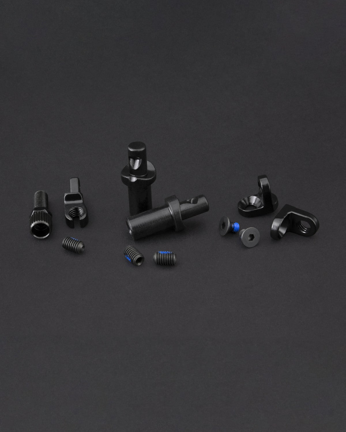 The Fly Bikes EBS Brake Mount Kit features small black mechanical components, including screws, nuts, and cylindrical parts, arranged on a dark surface—essential for any project.