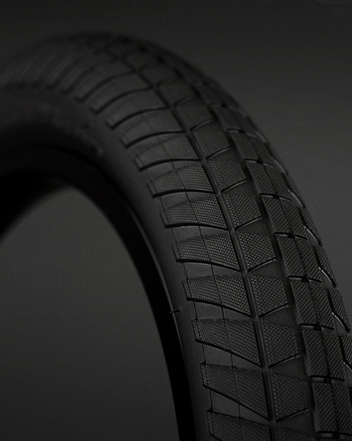 Close-up of a Fly Bikes Ruben Tyre STD bicycle tire with a textured tread pattern against a dark background, featuring 110 PSI and puncture-resistant technology for ultimate performance.