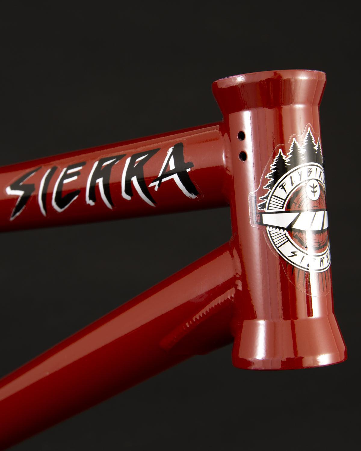 Close-up of a Fly Bikes Sierra Frame in red, made from durable 4130 CrMo steel, featuring the word "Sierra" and an emblem with trees on a stylish black background.