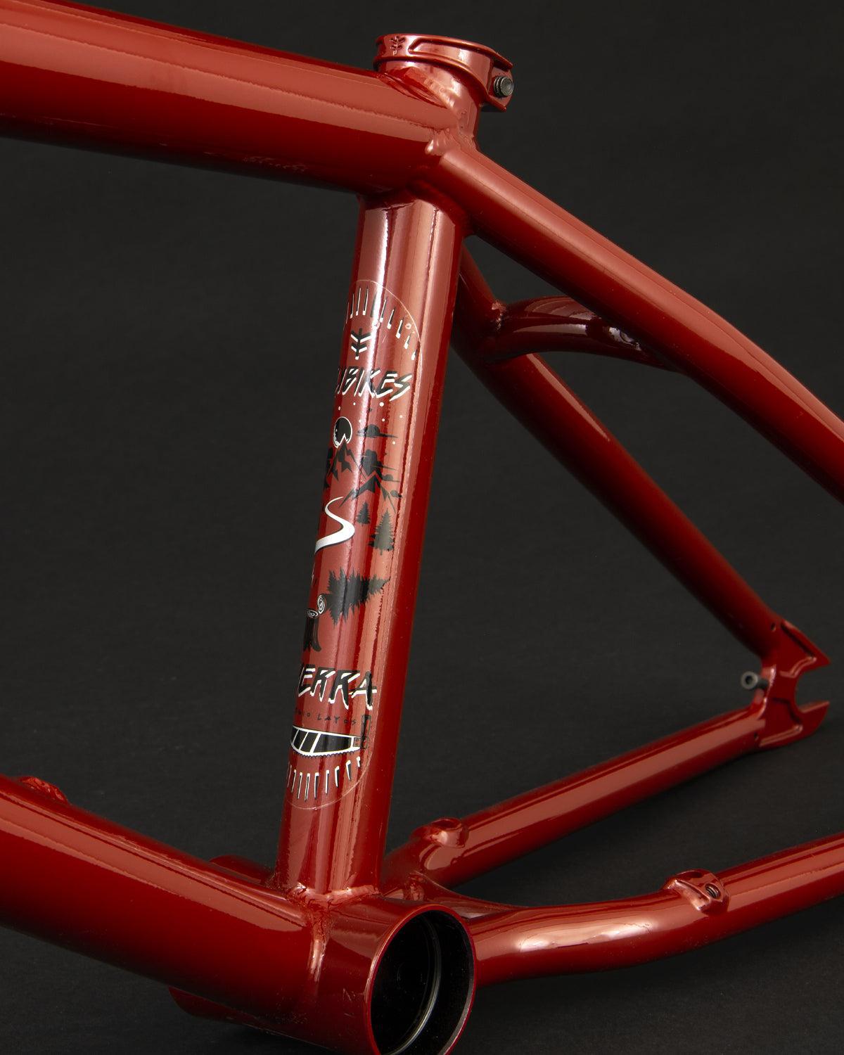 Close-up of a red Fly Bikes Sierra frame crafted from durable 4130 CrMo with a matte finish, featuring tree decals and "USA" on the vertical tube, against a black background.