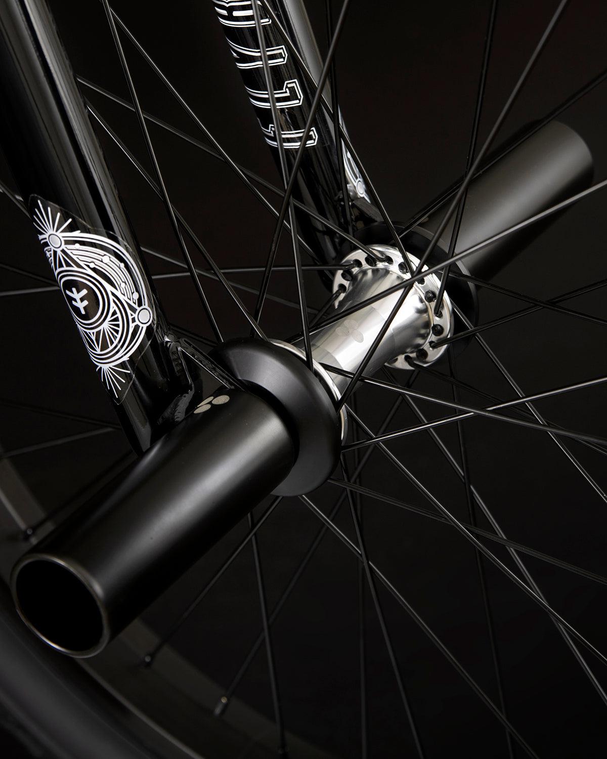 Close-up view of the Fly Bikes Proton CST 20 Inch Bike's wheel, showcasing black pegs attached to the axle, decorative patterns on the fork, and sealed hubs for a smooth ride.