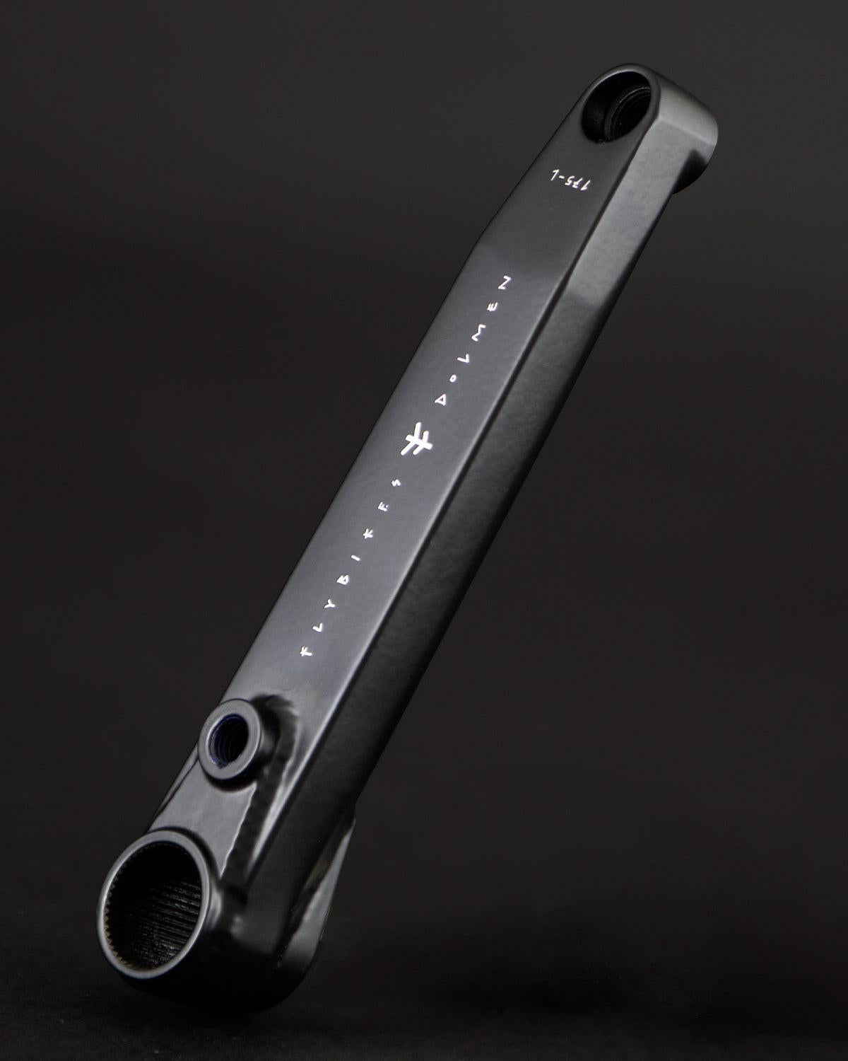 A black Fly Bikes Dolmen 24 crank arm, crafted from CNC machined 4130 Chromoly, is shown on a dark background with white markings and text highlighting its precision and durability.