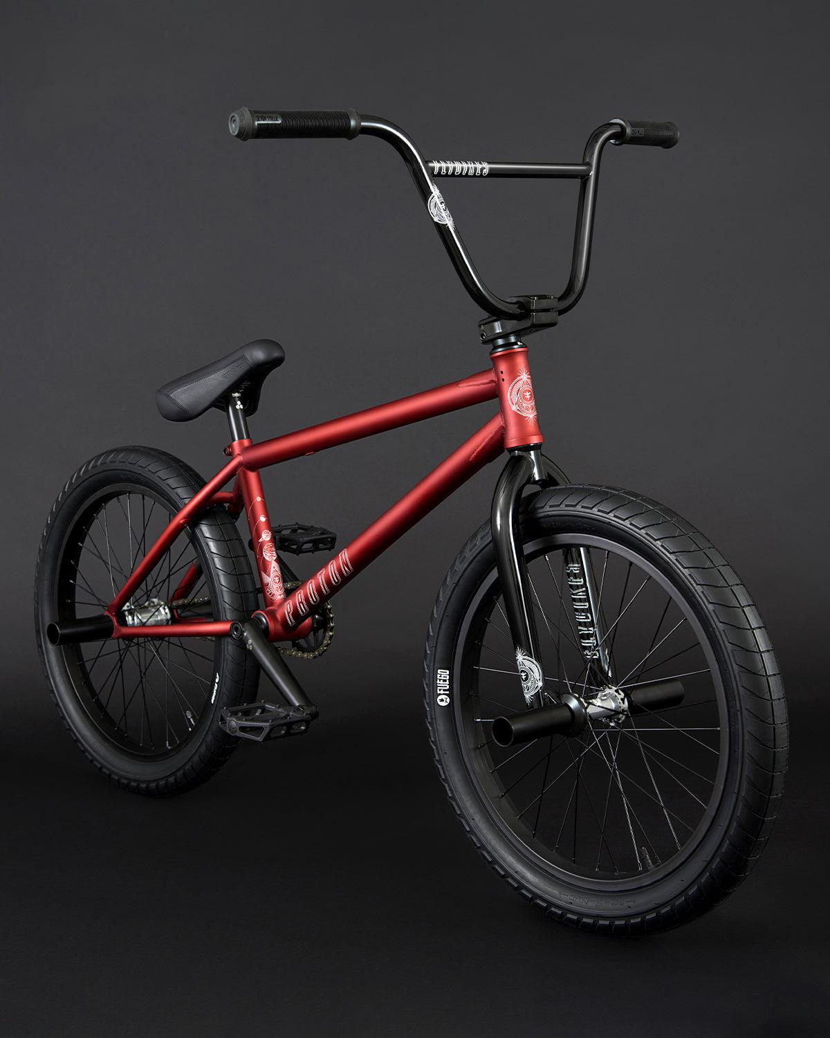 The Fly Bikes Proton CST 20 Inch Bike, featuring a red frame with black handlebars, sealed hubs, and thick tires, is showcased against a black background.