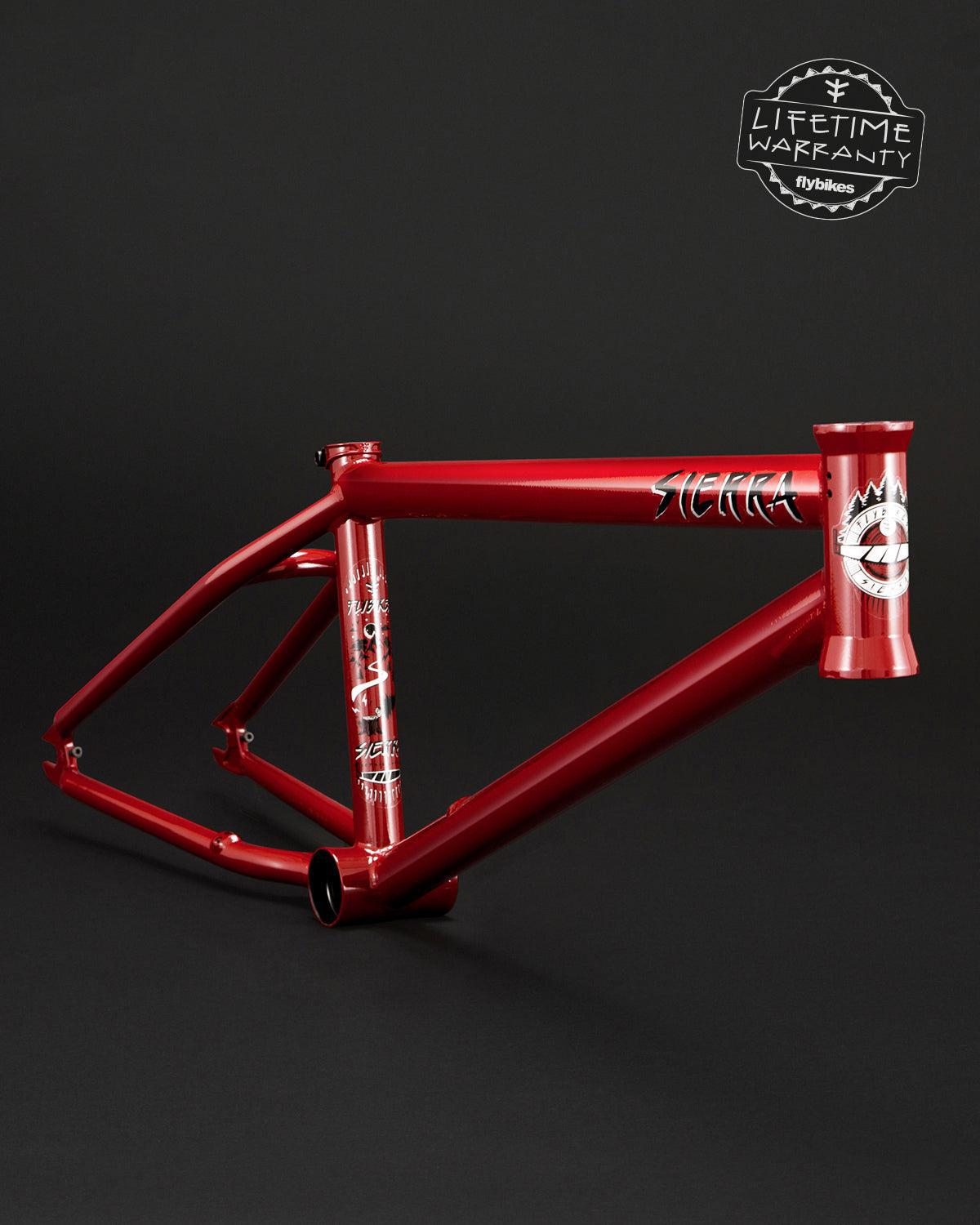 Fly Bikes Sierra Frame in red features a 4130 CrMo build with white graphics, a "Lifetime Warranty" badge on the top right, and Investment Cast components for enhanced durability against the stark black background.