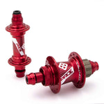 The Pride Control Expert 28H hubset in red features one hub standing upright and another lying on its side, highlighting the branded flanges and axle ends. These CNC machined aluminum hubs are expertly crafted for disc brakes, ensuring top performance on the track.