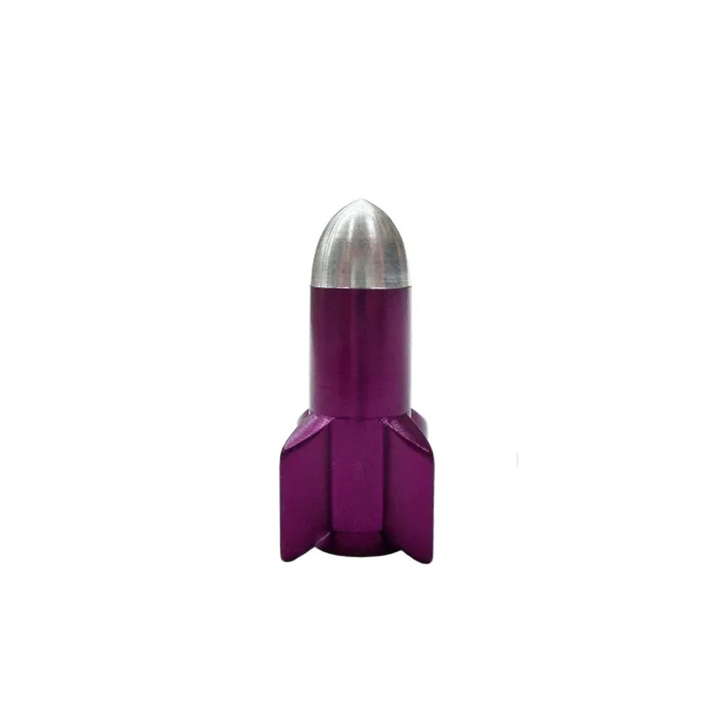 On a white background, a small metallic purple object with a silver tip and four fins at the base stands upright, resembling the sleek Guided Missile Valve Cap (pair), perfect as unique bike accessories.