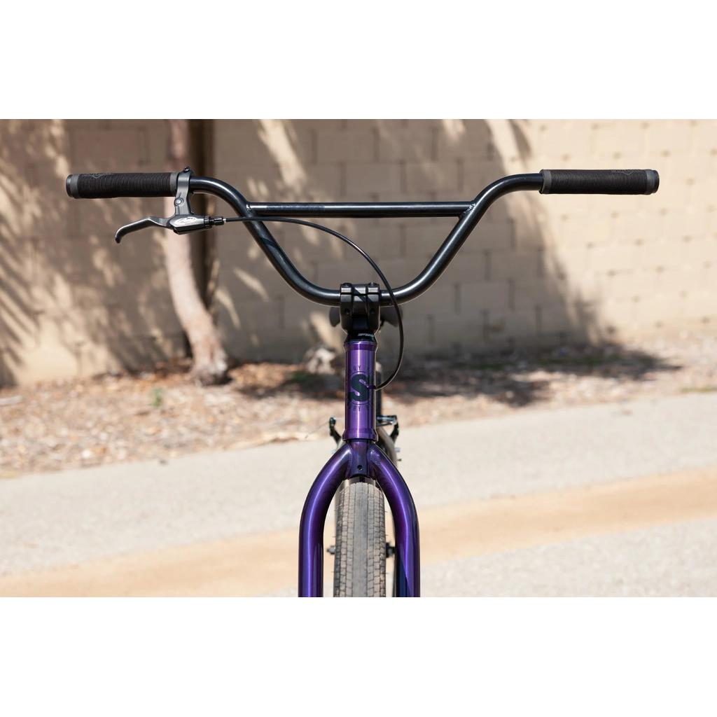 Front view of a Sunday High C 29 Inch Bike with purple chromoly frame and handlebars, black grips, a single brake lever, set against a blurred outdoor background.